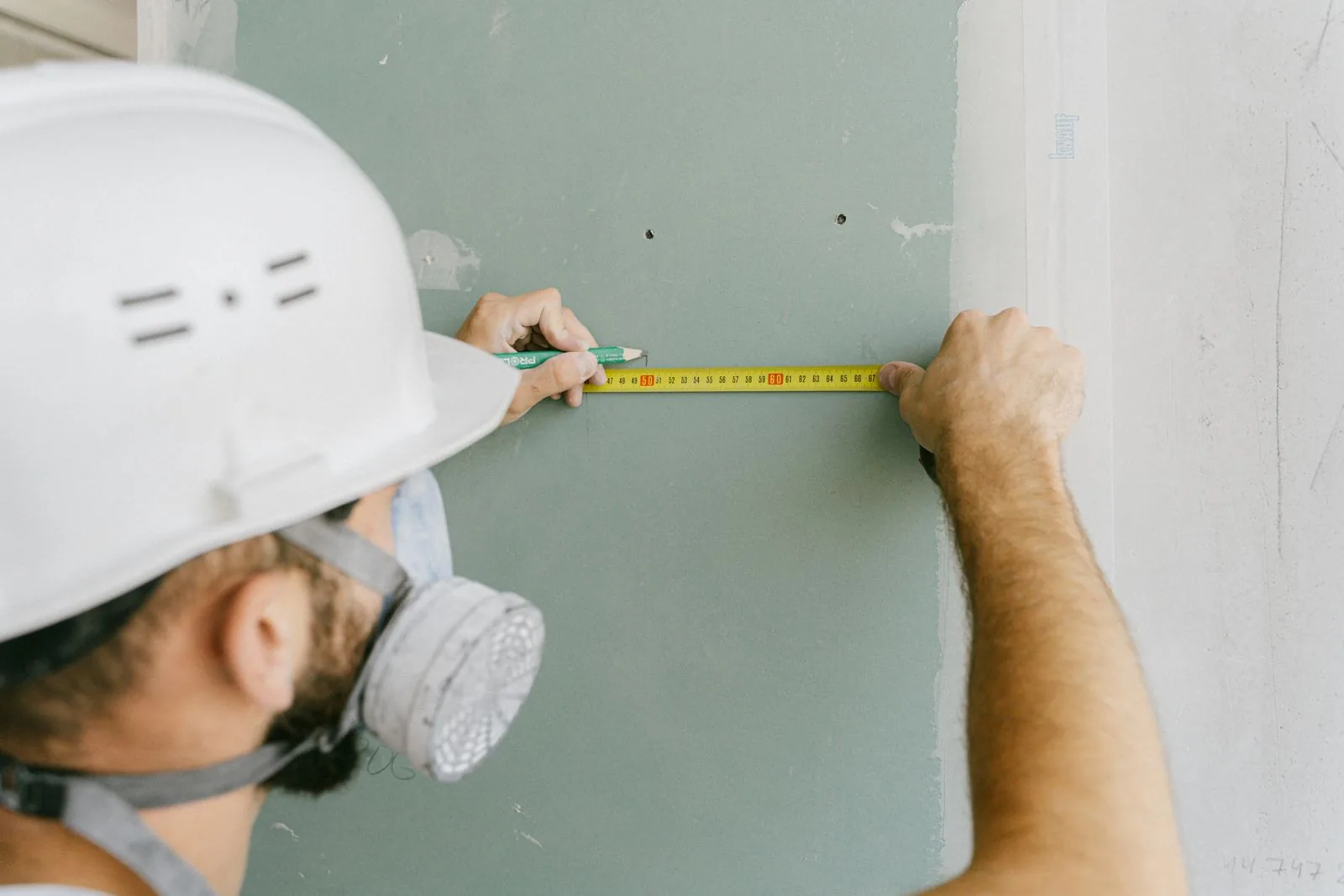 Worker measuring a wall while wearing a helmet and dust mask